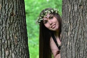 retrato de una joven emocional con una corona floral en la cabeza y adornos brillantes en la frente. linda morena posando en un hermoso bosque floreciente durante el día en un buen día foto