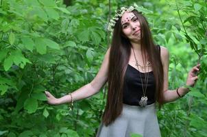 retrato de una joven emocional con una corona floral en la cabeza y adornos brillantes en la frente. linda morena posando en un hermoso bosque floreciente durante el día en un buen día foto