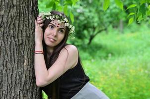 retrato de una joven emocional con una corona floral en la cabeza y adornos brillantes en la frente. linda morena posando en un hermoso bosque floreciente durante el día en un buen día foto