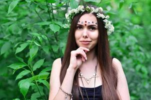 retrato de una joven emocional con una corona floral en la cabeza y adornos brillantes en la frente. linda morena posando en un hermoso bosque floreciente durante el día en un buen día foto