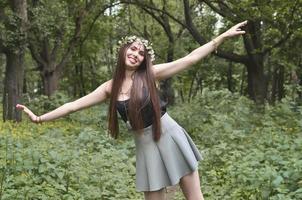 retrato de una joven emocional con una corona floral en la cabeza y adornos brillantes en la frente. linda morena posando en un hermoso bosque floreciente durante el día en un buen día foto