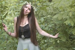 retrato de una joven emocional con una corona floral en la cabeza y adornos brillantes en la frente. linda morena posando en un hermoso bosque floreciente durante el día en un buen día foto