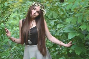 retrato de una joven emocional con una corona floral en la cabeza y adornos brillantes en la frente. linda morena posando en un hermoso bosque floreciente durante el día en un buen día foto