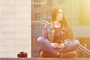 A girl photographer uses a smartphone and sits on a granite para photo