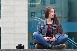 A girl photographer uses a smartphone and sits on a granite para photo