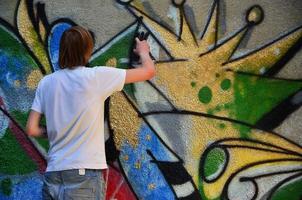 foto en el proceso de dibujar un patrón de graffiti en un antiguo muro de hormigón. un joven rubio de pelo largo dibuja un dibujo abstracto de diferentes colores. concepto de arte callejero y vandalismo