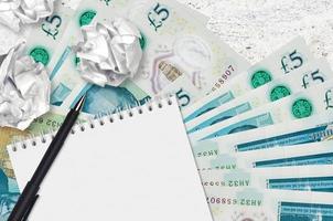 5 British pounds bills and balls of crumpled paper with blank notepad. Bad ideas or less of inspiration concept. Searching ideas for investment photo