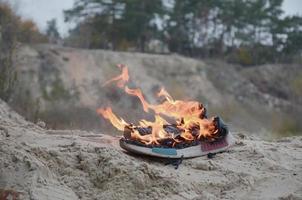 Burning sports sneakers or gym shoes on fire stand on sandy beach coast. Athlete burned out. Physical exertion during training concept photo