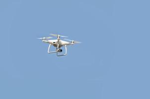 Big white drone hovering in a bright cloudless blue sky photo