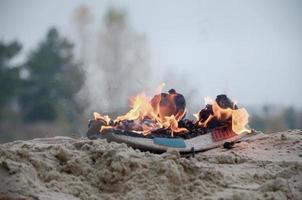 Burning sports sneakers or gym shoes on fire stand on sandy beach coast. Athlete burned out. Physical exertion during training concept photo