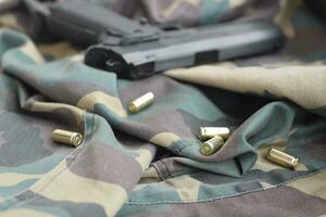 9mm bullets and pistol lie on folded camouflage green fabric. A set shooting range items or a self-defense kit photo