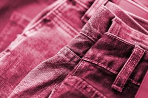 Many jeans in stack in wardrobe room. Row of pants denim jeans in closet. Concept of buy, sell, shopping and fashionable clothes Image toned in Viva Magenta, color of the 2023 year photo