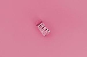 Stainless steel grater lies on a paper. Kitchen accessories. Tools for cooking. Image toned in Viva Magenta, color of the 2023 year photo