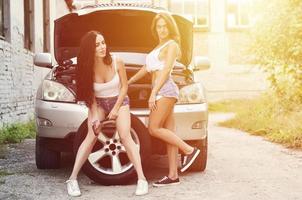 Two young and sexy girls with wheel wrenches around a silvery ca photo
