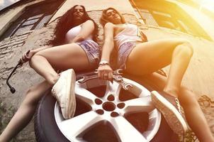 Two young and sexy girls with wrenches are sitting on the car wh photo