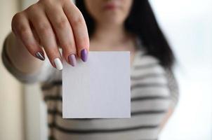 Young sad girl shows a white sticker. Caucasian brunette holding a blank sheet of paper as a template for your text photo