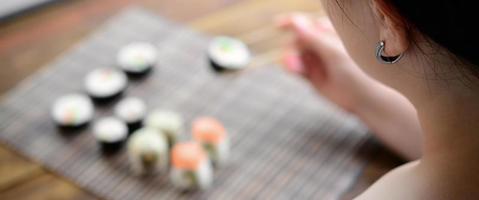 una chica morena con palillos sostiene un rollo de sushi sobre un fondo de alfombra de paja de bambú. comida asiática tradicional foto