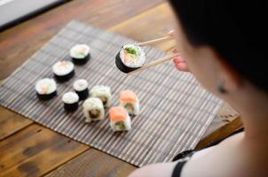 Brunette girl with chopsticks holds a sushi roll on a bamboo straw serwing mat background. Traditional Asian food photo