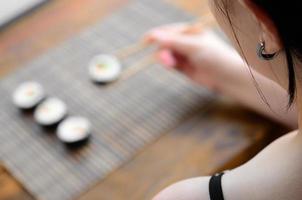 una chica morena con palillos sostiene un rollo de sushi sobre un fondo de alfombra de paja de bambú. comida asiática tradicional foto