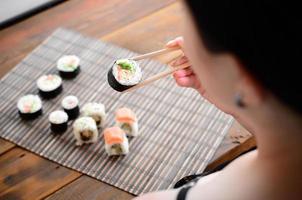 Brunette girl with chopsticks holds a sushi roll on a bamboo straw serwing mat background. Traditional Asian food photo