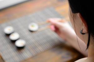 una chica morena con palillos sostiene un rollo de sushi sobre un fondo de alfombra de paja de bambú. comida asiática tradicional foto