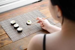 una chica morena con palillos sostiene un rollo de sushi sobre un fondo de alfombra de paja de bambú. comida asiática tradicional foto