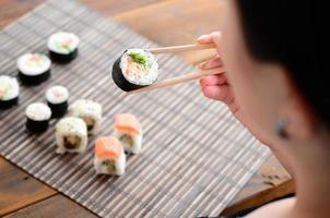 una chica morena con palillos sostiene un rollo de sushi sobre un fondo de alfombra de paja de bambú. comida asiática tradicional foto