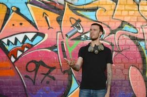 Young graffiti artist with gas mask on his neck throw his spray can against colorful pink graffiti on brick wall. Street art and contemporary painting process photo