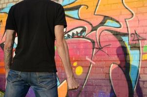 Back view of young caucasian man with brass cnuckle on his hand against ghetto brick wall with graffiti paintings. Concept of criminal forces and aggression charge photo
