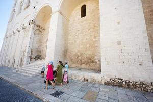 familia de turistas caminando contra la basílica de san nicolás en bari, puglia, sur de italia. foto