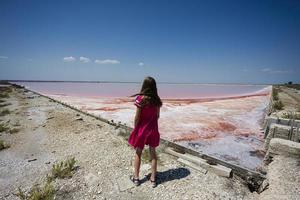 Girl in pink dress against red salt lake in Saline Margherita di Savoia of Italy. photo