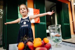 Happy baby girl against italian flag celebrating Republic Day of Italy and eat fruits. photo