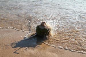 Travel to island Phuket, Thailand. A coconut with straw on the sandy beach near to the sea in the sunny weather. photo