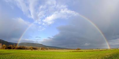 arco iris sobre nubes de lluvia oscuras sobre campos verdes en el panorama invernal foto