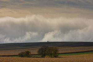 fields with a wayside shrine  a huge dense wall of white fog on the ground photo