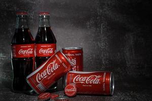 Ayutthaya, Thailand-25June2020- Coca-Cola Classic in a glass bottle and can on dark toned cement Background. Coca Cola, Coke is the most popular carbonated soft drink beverages sold around the world photo