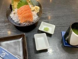 varios menús, sushi, sashimi, nigiri, cerdo frito y sopa de miso. sashimi, chutoro sashimi, palillos de comida japonesa y wasabi en la mesa negra, estilo de comida japonesa. desdibuja el foco. foto