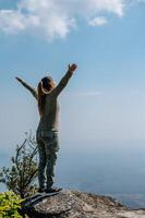 Young trekking woman standing on rocky mountain peak photo