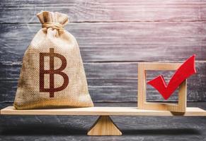 Red vote tick and a thai baht money bag on scales. Estimating cost of making a decision and consequences in the future. Concept of lobbying for decisions and laws. Corruption risks. photo