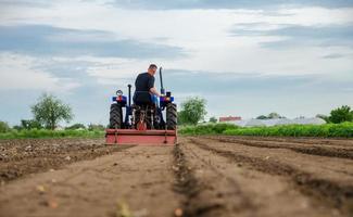 A farmer drives a tractor and cultivates an agricultural field. Milling soil, crushing before cutting rows. Farming, agriculture. Loosening surface, land cultivation. Plowing field. photo