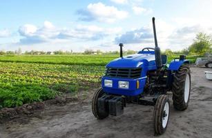 tractor azul sin conductor cerca de un campo agrícola. maquinaria y tecnología agrícola. organización de actividades agrícolas, planificación empresarial. apoyo a los agricultores con subsidios y préstamos. foto