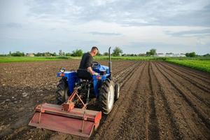 A farmer cultivates a field with a tractor after harvest. Milling soil, crushing before cutting rows. Farming, agriculture. Loosening surface, land cultivation. Plowing field. Removing roots photo