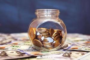 Glass jar with coins on the black background. A lot of dollar bills photo