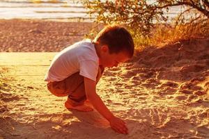 boy playing with sand on the beach. sunset photo