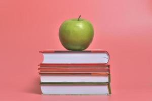 manzana verde en los libros aislado sobre fondo de color rosa foto