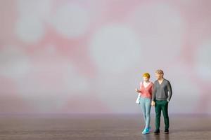 Miniature people man and woman in casual cloth standing together on pink background photo