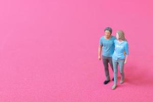 Miniature people man and woman in casual cloth standing together on pink background photo