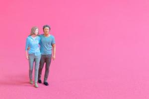 Miniature people man and woman in casual cloth standing together on pink background photo