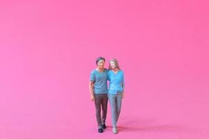 Miniature people man and woman in casual cloth standing together on pink background photo