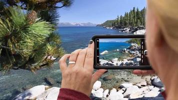 Cinemagraph en bucle de 4k de una mujer filmando el paisaje de la orilla del lago en un teléfono inteligente video